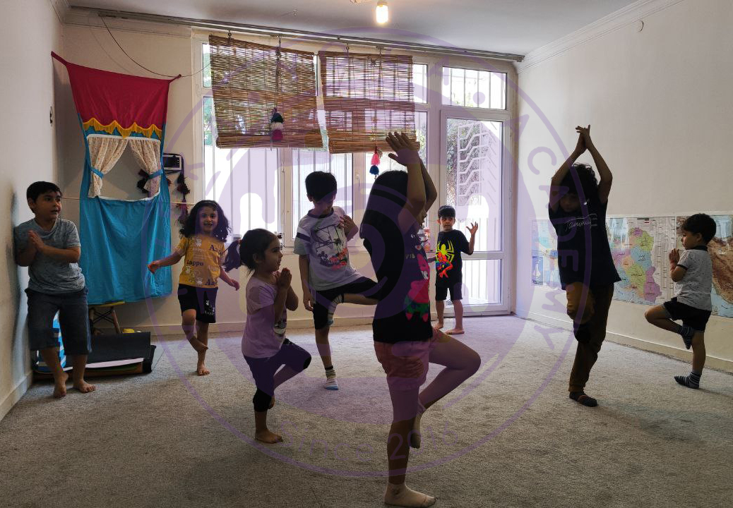 کودک در حال ایستادن در حالت درخت (Vrikshasana) در کلاس یوگا